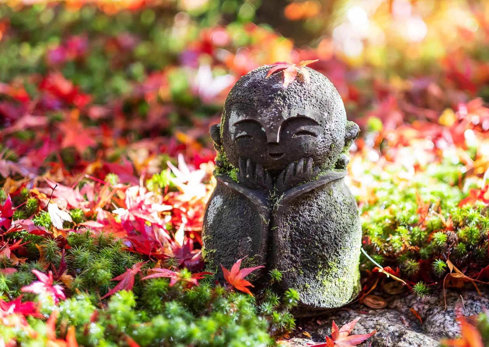 Japanische Jizō-Skulptur mit herabfallendem roten Ahornblatt im Garten des Enkō-ji-Tempels in Kyoto, Japan