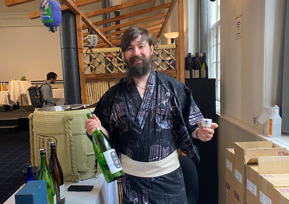 Jeremy hält eine Sake-Flasche und –Tasse in den Händen.