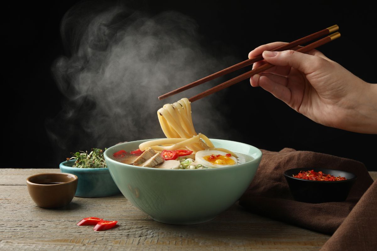 Frau isst Ramen mit Stäbchen am Holztisch