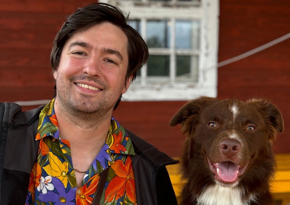 Jeremy Batt sitzt lächelnd neben einem braun-weißen Hund an einem Holztisch.