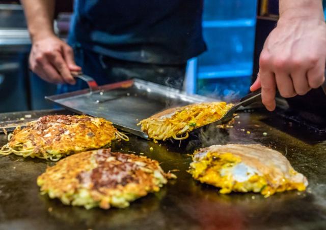 Japanische Okonomiyaki beim Kochen auf einer Heizplatte 