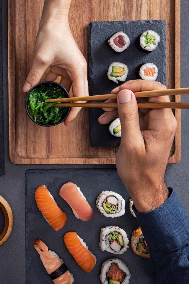 Verschiedene Sushi wie Nigiri, Sashimi und Rollen werden geteilt und mit Stäbchen gegessen