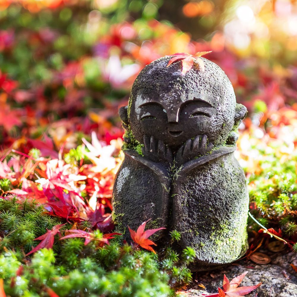 Japanische Jizō-Skulptur mit herabfallendem roten Ahornblatt im Garten des Enkō-ji-Tempels in Kyoto, Japan